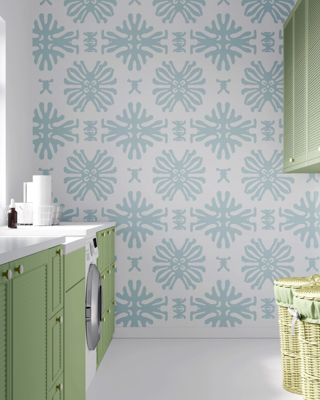 A styled laundry room scene showing a wall covered in a repeating light blue and white Bali ornamental pattern, with green cabinets along the left side and a wicker basket on the right.