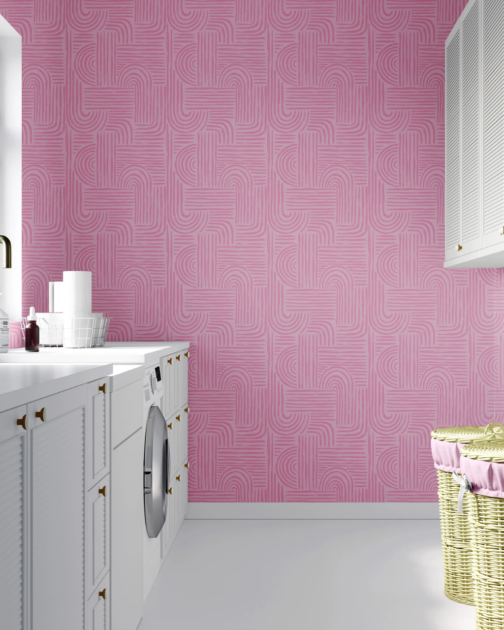 Pink geometric Verona patterned wallpaper on a wall in a bright, modern laundry room with white cabinets, a washing machine, and a yellow wicker basket.